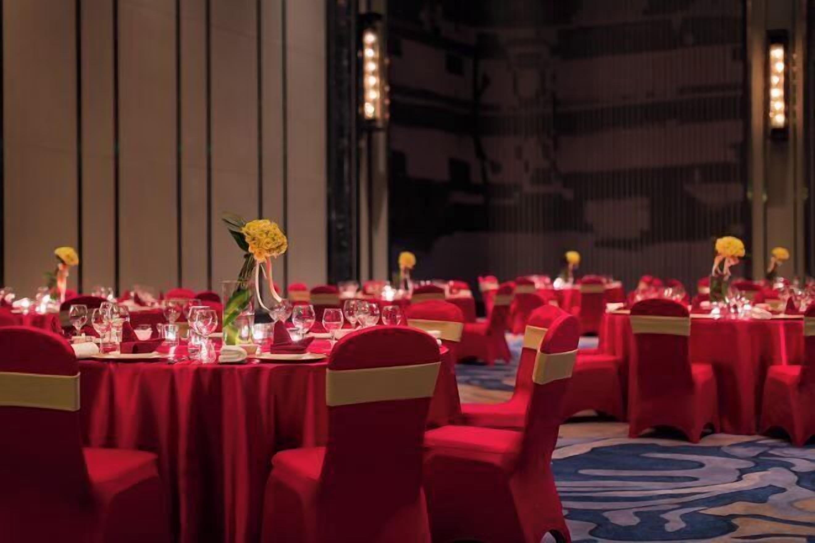 Un salón de banquetes con mesas redondas, sillas rojas y centros de mesa con flores amarillas.