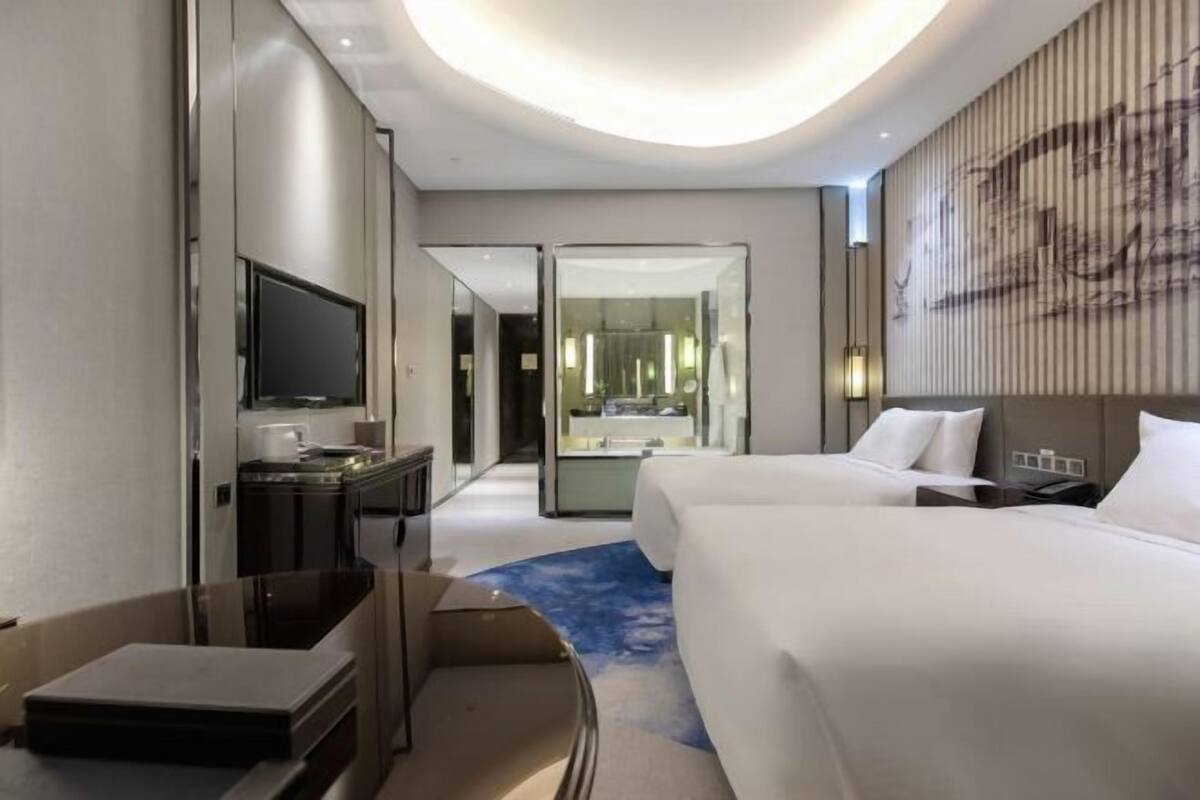 A modern hotel room with a flat-screen TV, a desk, a bed, and a bathroom with a glass partition.