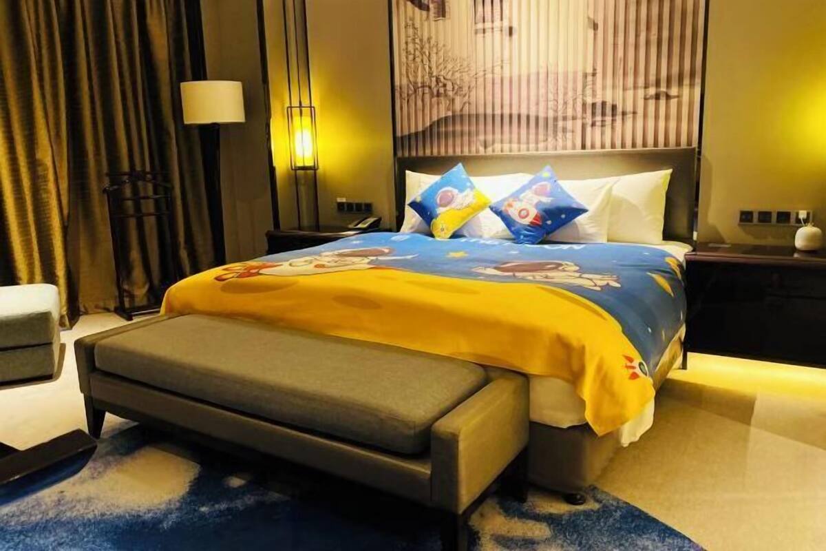 A hotel room with a bed, bedside tables, a lamp, and a window with blinds.