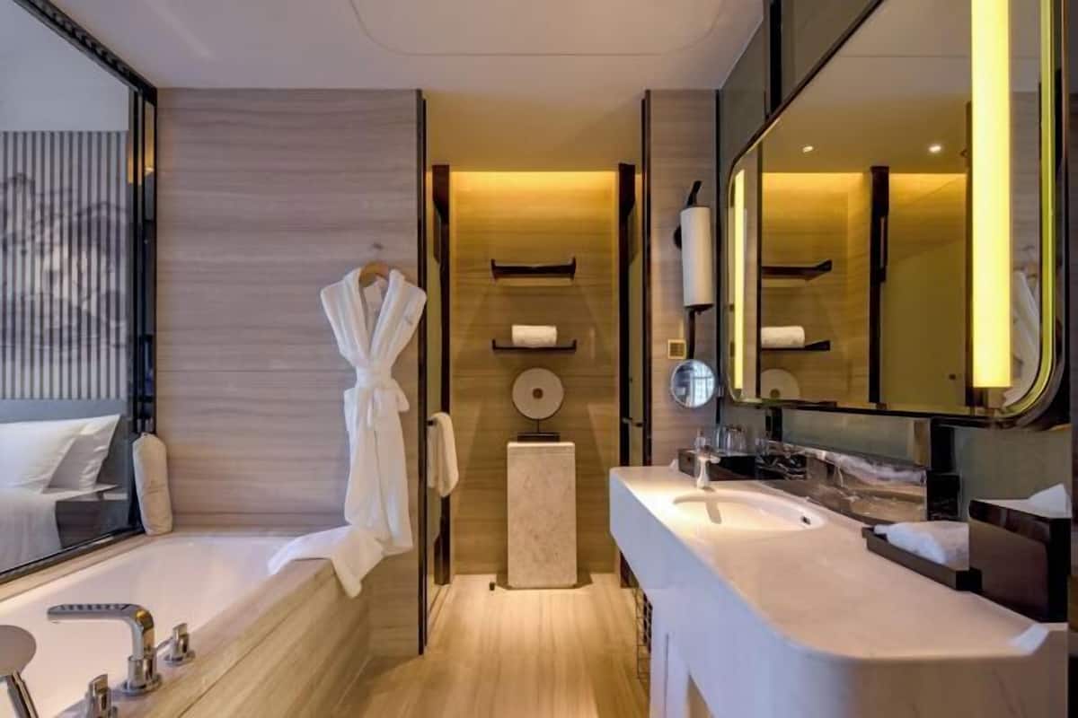 A modern bathroom with a bathtub, two sinks, a large mirror, and a towel rack.