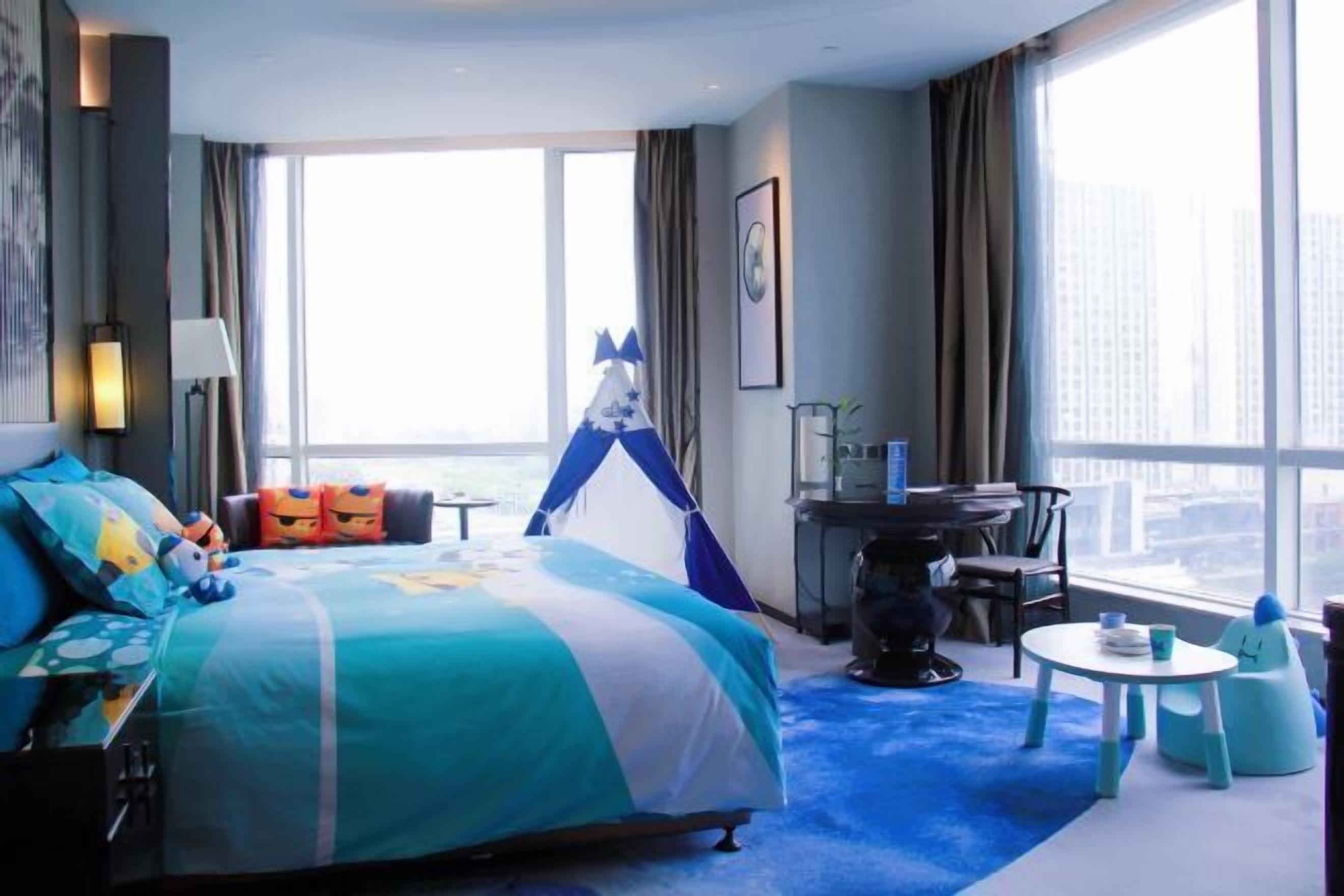 Habitación de hotel con cama, escritorio, silla, una mesita y ventana con vista a la ciudad.