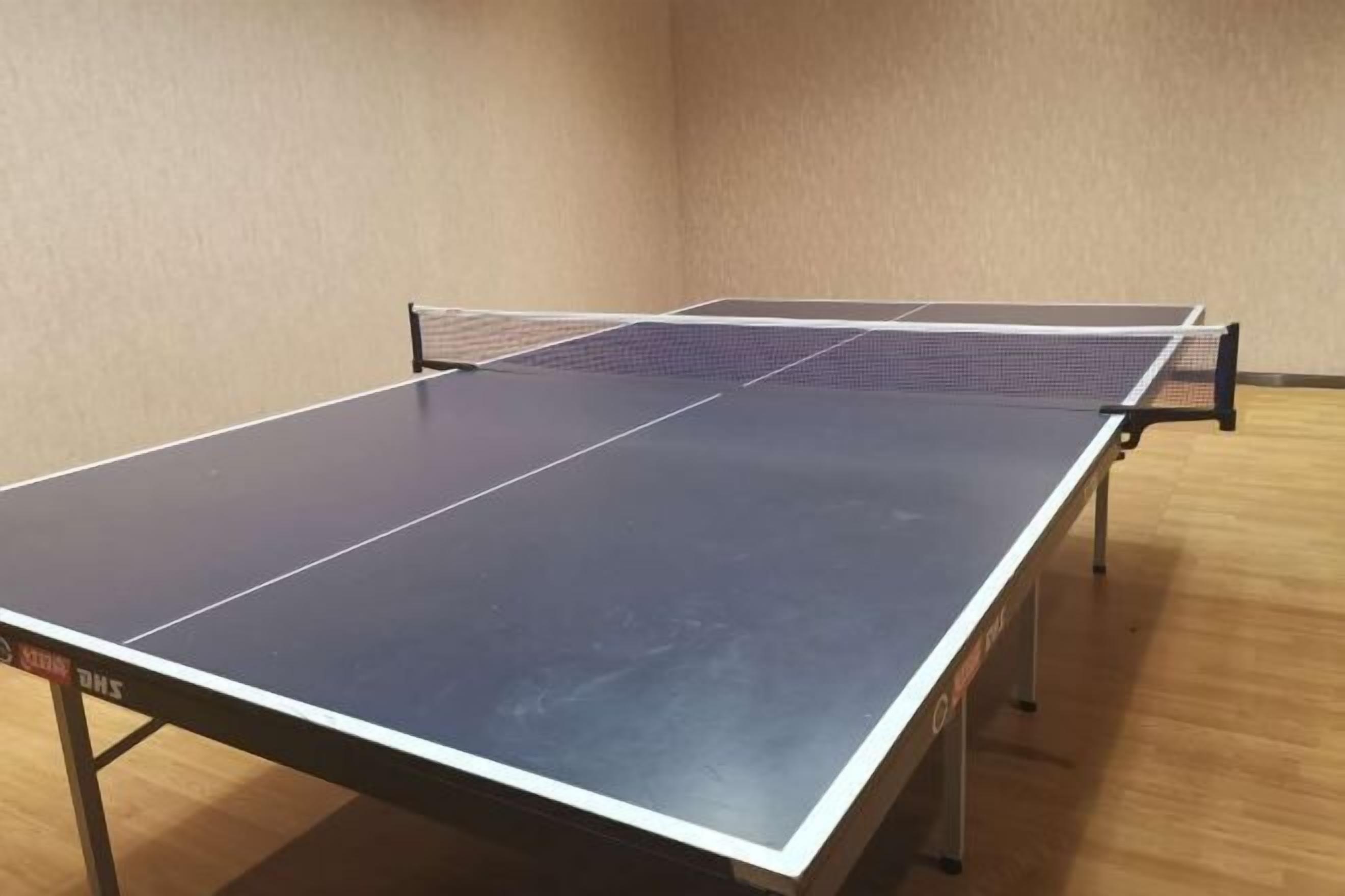 A ping pong table in a room with wooden flooring and beige walls.