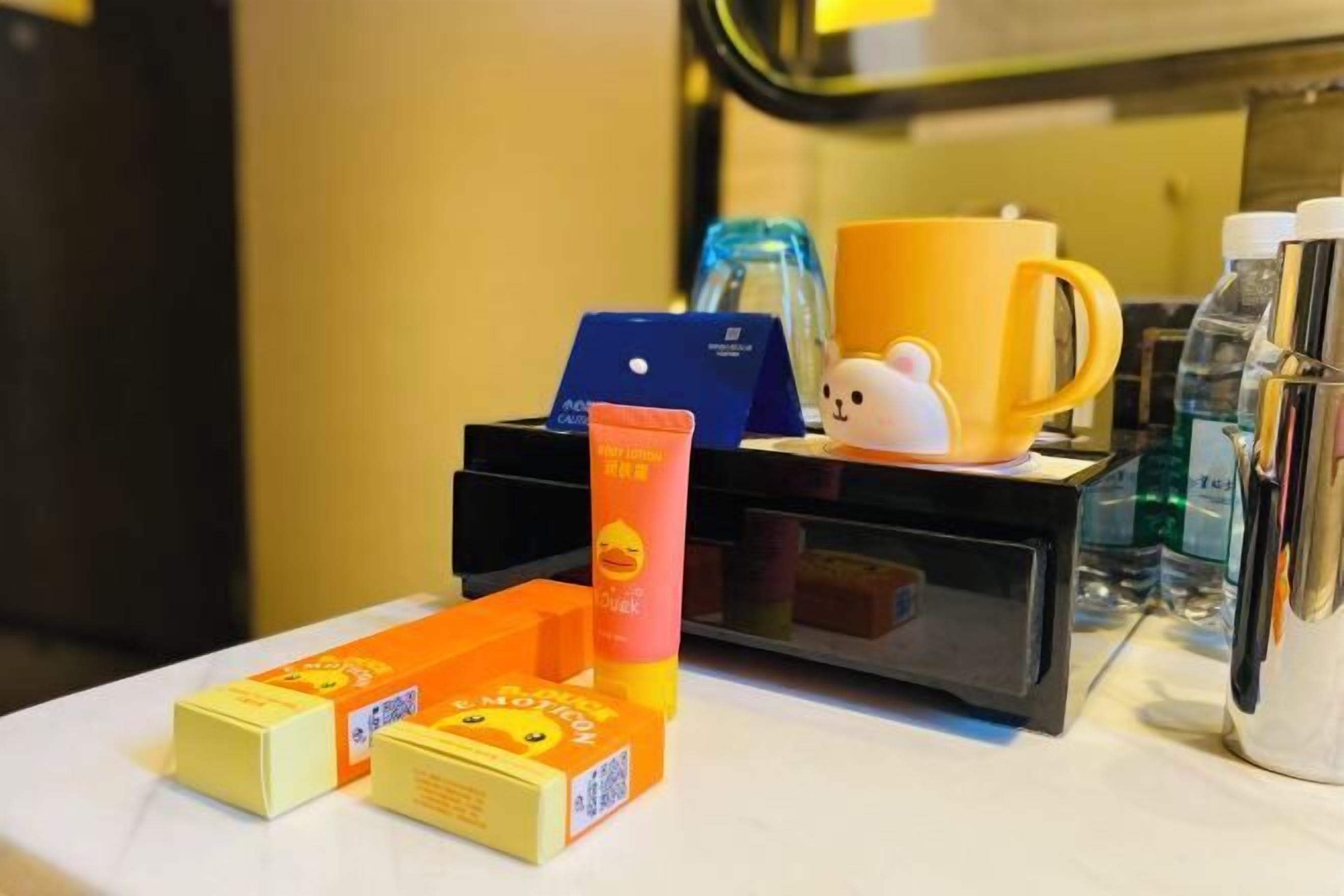 A hotel room with a minibar, a small table with toiletries, a coffee maker, and a decorative mug.