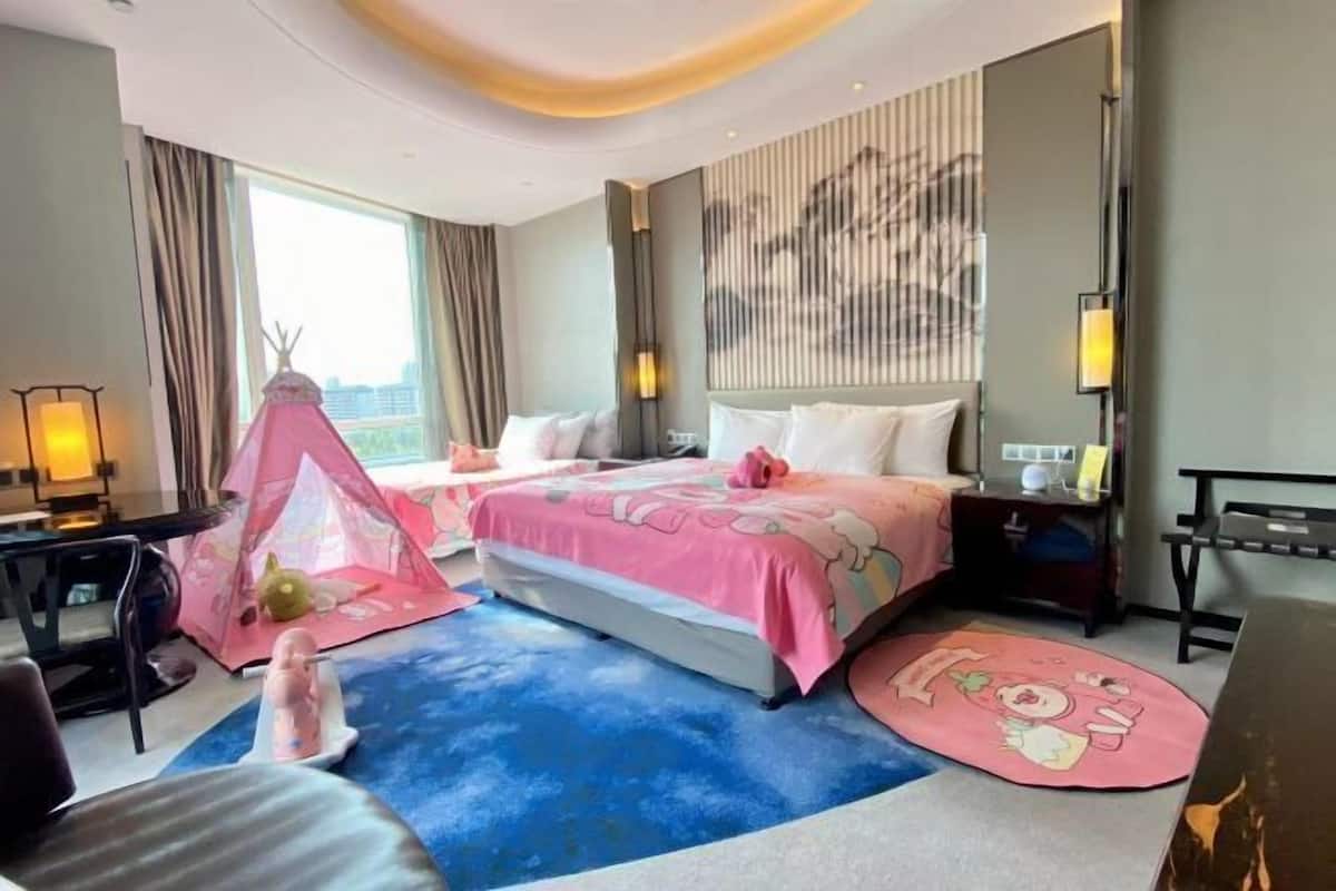 A hotel room with a bed, a desk, a chair, a tent, and a view of the city.