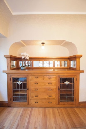 Un mueble de madera con puertas de cristal y cajones, una lámpara arriba y un jarrón con flores encima.