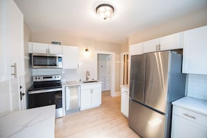 Una cocina moderna con armarios blancos, electrodomésticos de acero inoxidable y piso de madera clara.