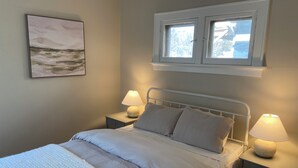 Makuuhuone, jossa on sänky, kaksi yöpöytää valaisimineen, ikkuna, josta on näkymä, ja taulu seinällä.