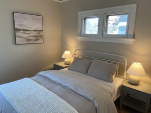 Un dormitorio con cama, dos mesitas de noche con lámparas, una ventana con vistas y un cuadro en la pared.