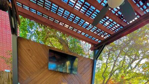 An outdoor seating area with wicker furniture and a TV screen on the wall. - Backyard Oasis! (San Antonio)
