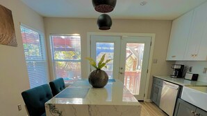 A modern kitchen with a marble island, black pendant lights, and a view through the glass doors. - Backyard Oasis! (San Antonio)