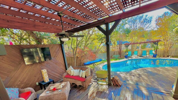 A covered outdoor deck with wicker furniture, a ceiling fan, and a pool. - Backyard Oasis! (San Antonio)