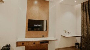 A modern bathroom with a wooden vanity, a mounted television displaying 'android', and a small shelf with a vase. - Banmali Palaces  (Titilagarh)