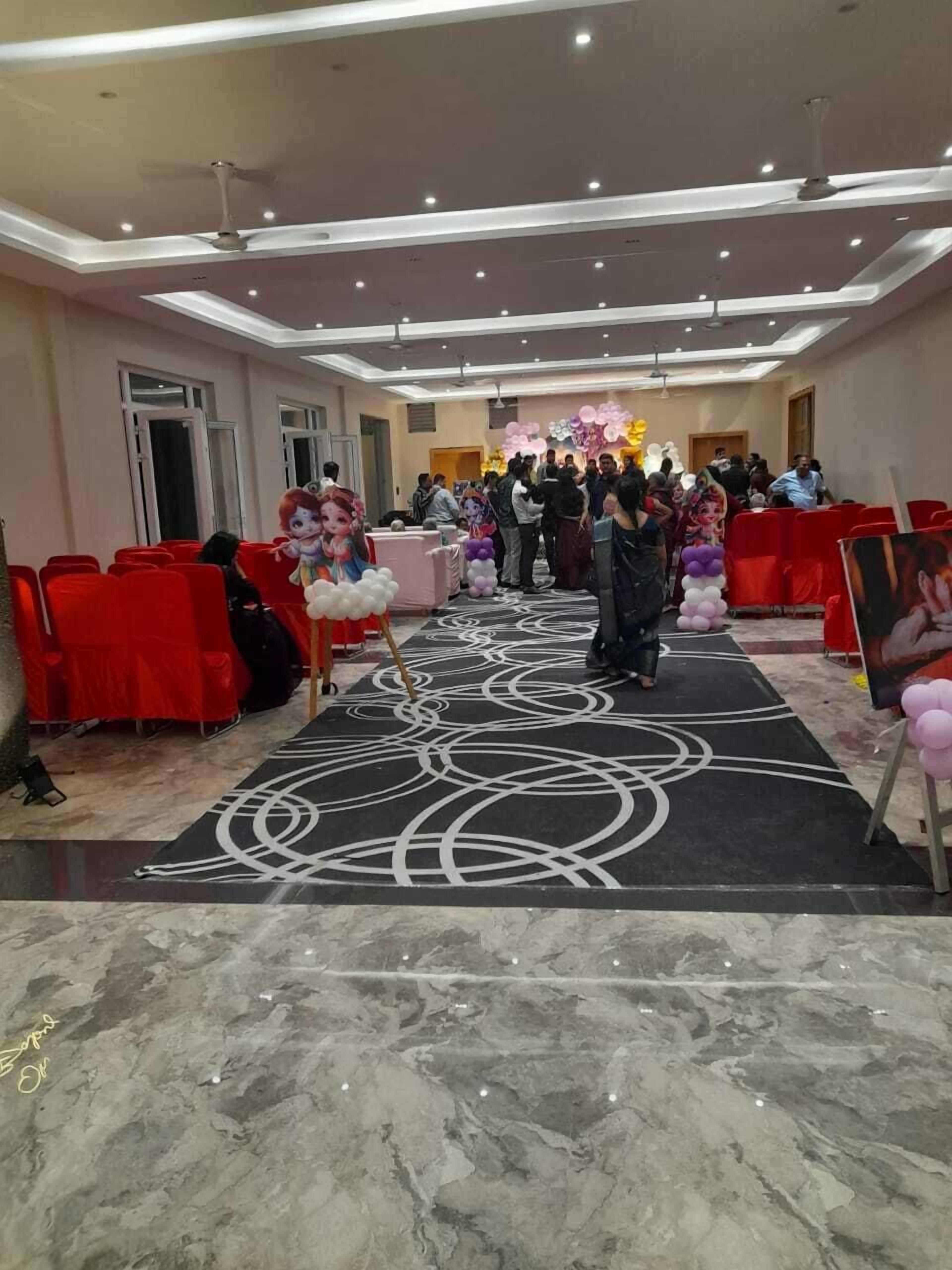 Un vestíbulo de hotel con sillas rojas, una alfombra negra con diseños blancos e iluminación empotrada en el techo.
