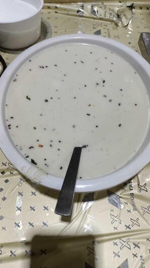 A bowl of soup with a spoon, placed on a table with a patterned tablecloth. - Banmali Palaces  (Titilagarh)