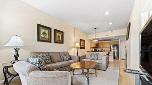 A living room with a sofa, armchairs, a coffee table, and a TV. There is a kitchen in the background. - Gac217c1 (Copper Mountain)