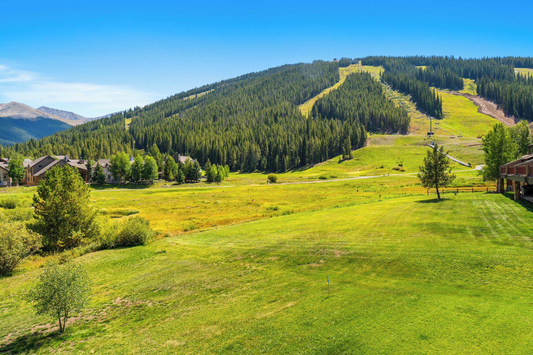 A rural landscape with houses, green fields, and a forested hill.