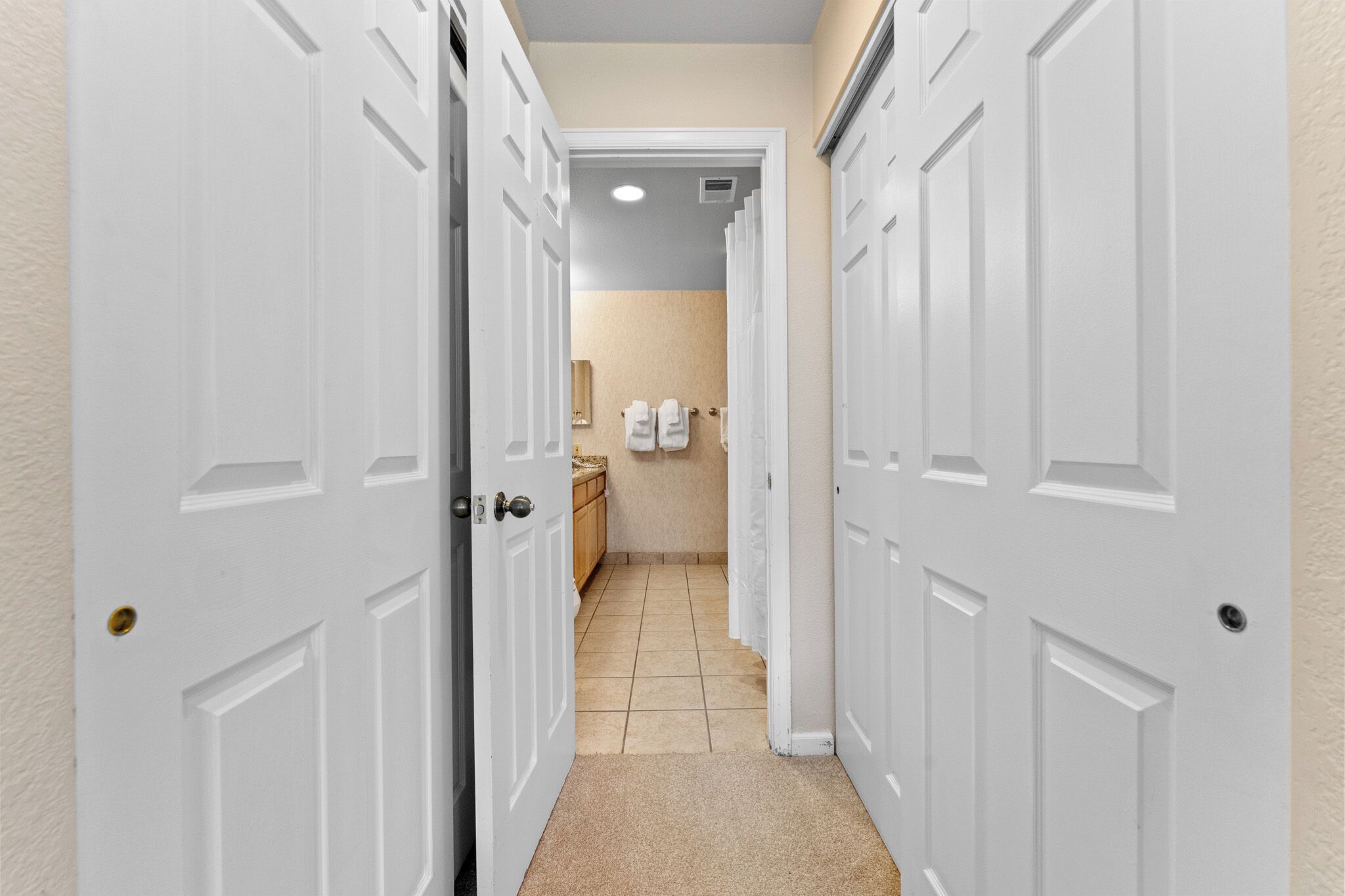 A narrow hallway with white doors leading to a bathroom.
