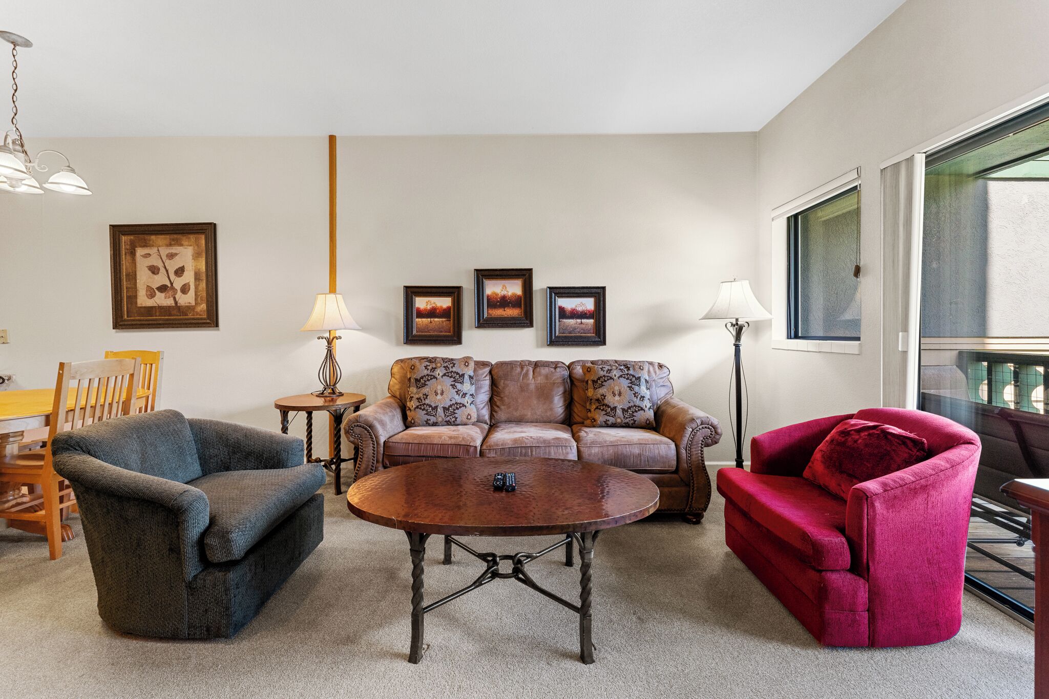A living room with a brown leather sofa, a blue armchair, a red armchair, a coffee table, and a dining table with chairs.