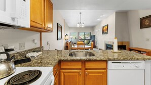 A kitchen with granite countertops, wooden cabinets, a built-in dishwasher, and a dining area with a table and chairs. - Gac316c2 (Copper Mountain)
