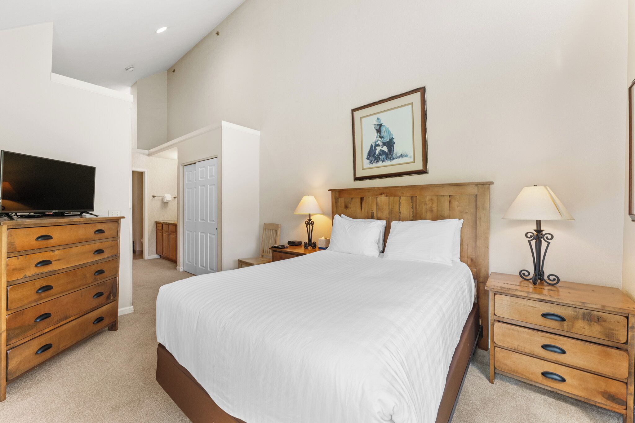 A bedroom with a large bed, wooden nightstands, a television, and a framed picture on the wall.