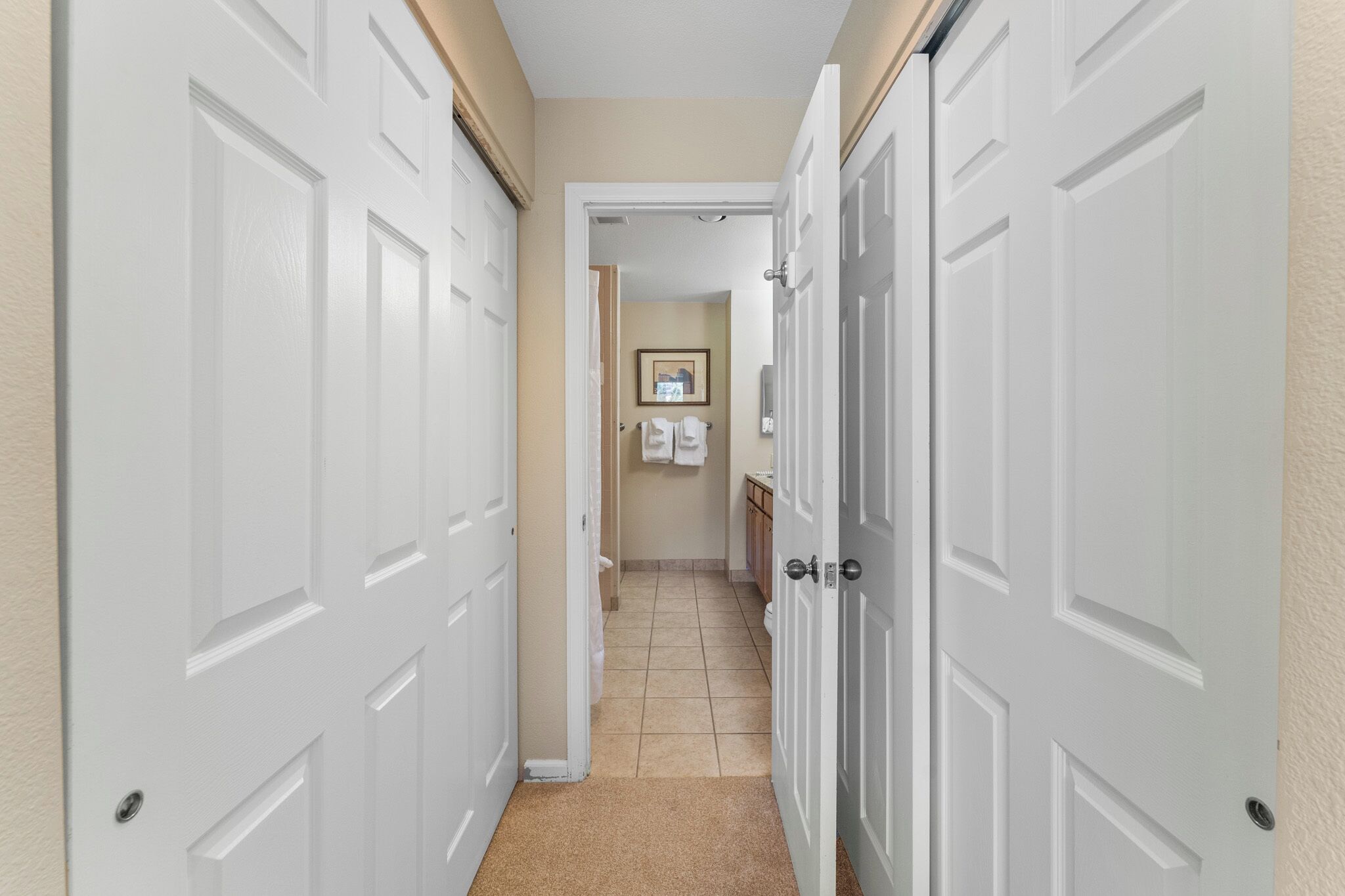 A narrow hallway with white doors leading to a bathroom and a kitchen area.