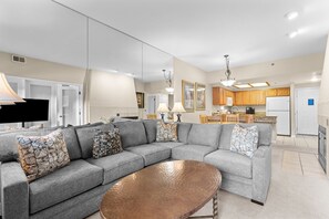 A modern living room with a grey sectional sofa, a coffee table, and a kitchen area with wooden cabinets and a refrigerator. - Greens at Copper #315 By Summit County Mountain Retreats (Copper Mountain)