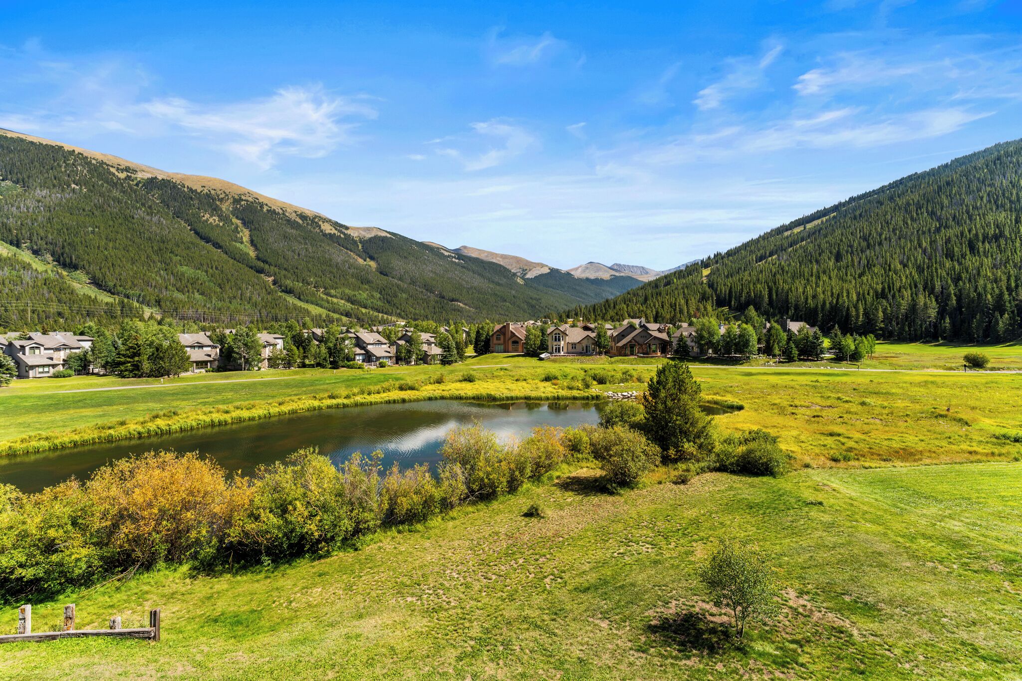 Una vista panoràmica d'una zona residencial amb cases, un estany i muntanyes al fons.
