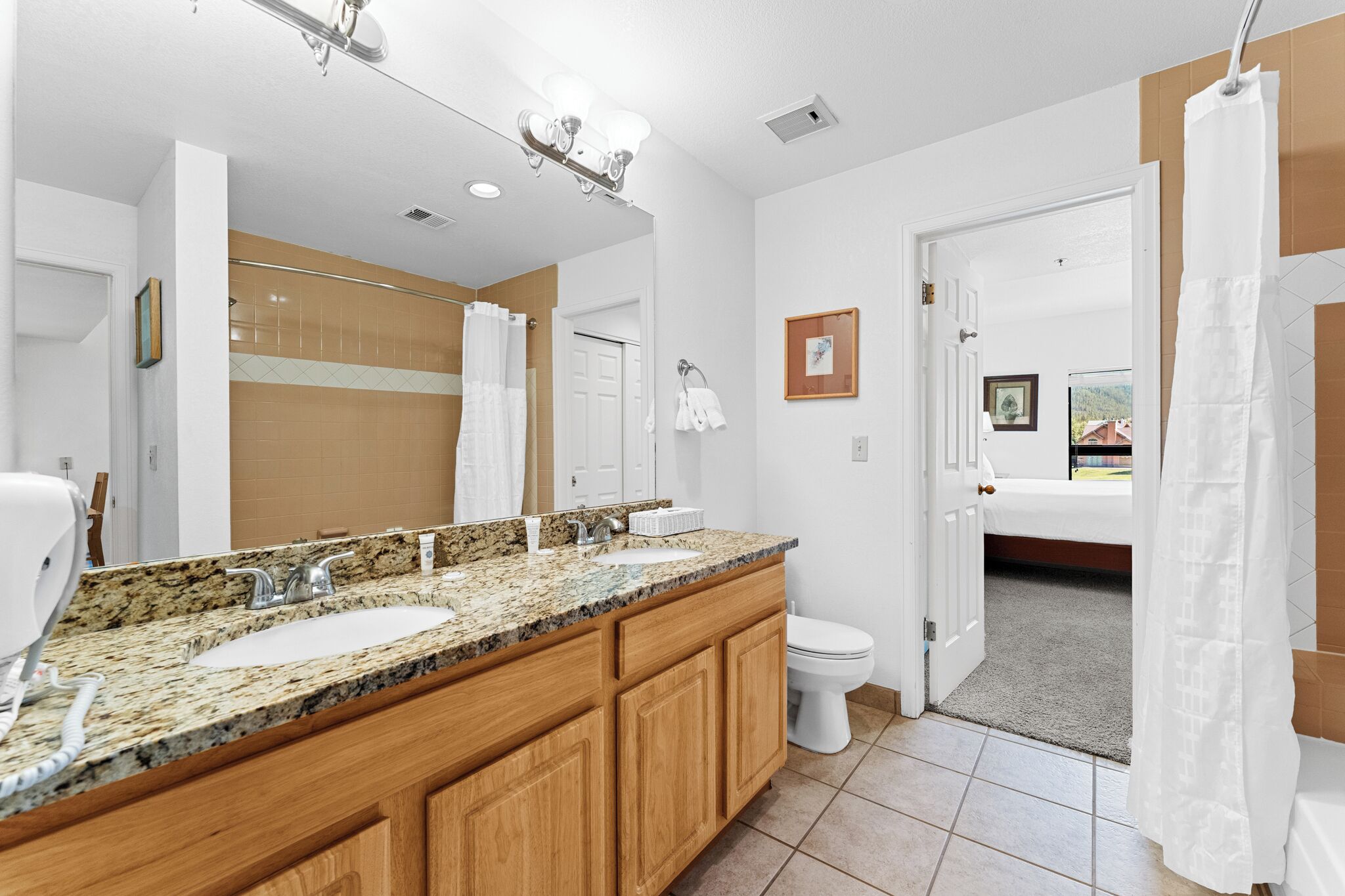 A modern bathroom with a granite countertop, two sinks, a mirror, and a toilet.