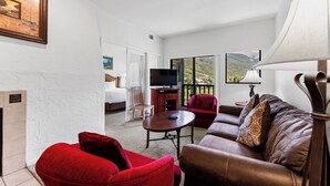 A hotel room with a large bed, a TV, a red armchair, a brown sofa, and a view of a mountainous landscape through large windows. - Gac317c2 (Copper Mountain)