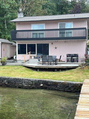 A two-story house with a deck, outdoor furniture, and a stone wall. - Quaint Lakefront Cottage w/Hot tub In Bellingham (Bellingham)