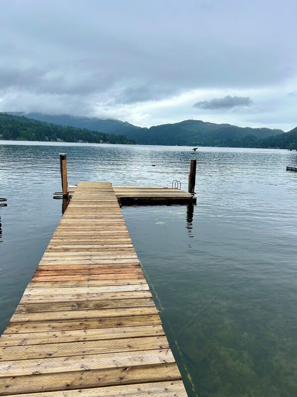 A wooden pier extending into calm water with a forested mountain backdrop.