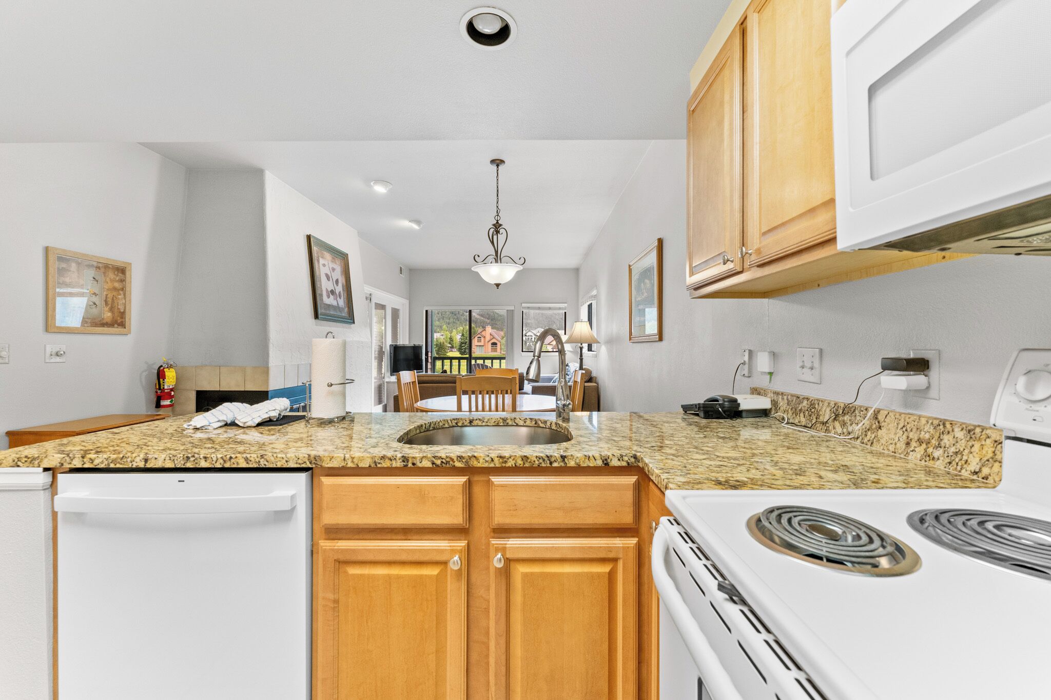 A modern kitchen with granite countertops, wooden cabinets, a built-in dishwasher, and a white stove.
