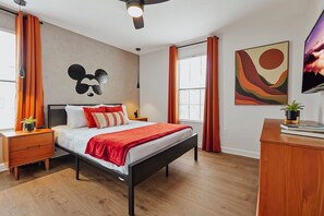 A modern bedroom with a bed, nightstands, a desk, a ceiling fan, and artwork on the walls.