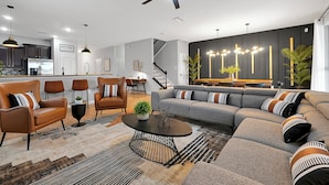 A modern living room with a sectional sofa, two armchairs, a coffee table, and a dining area with a kitchen in the background.