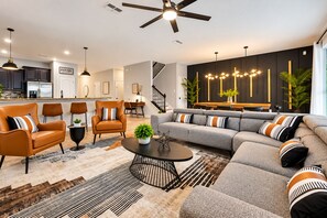 A modern living room with a sofa, armchairs, a coffee table, and a dining area with a staircase.
