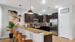 A modern kitchen with dark cabinets, a granite countertop, stainless steel appliances, and a bar area with stools.