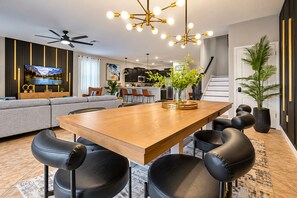 A modern living room with a wooden dining table, black leather chairs, a television, and a ceiling fan.