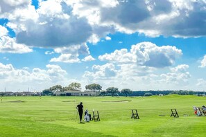 A golf course with a clear sky, a golfer, and a clubhouse in the background.