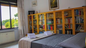 A bedroom with a bed, a window with curtains, a radiator, and a bookshelf filled with books. - Panoramic in the Hillside surrounded by greenery (Moncalieri)