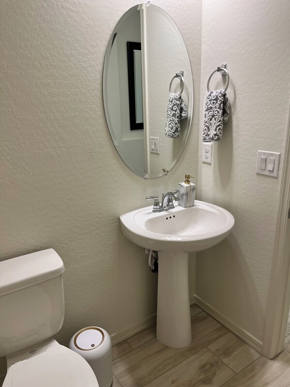 A bathroom with a white sink, a mirror, a toilet, and a towel rack with patterned towels.