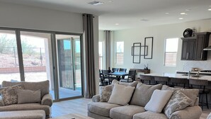 A spacious living room with a large sofa set, a coffee table, and a dining area with a table and chairs.