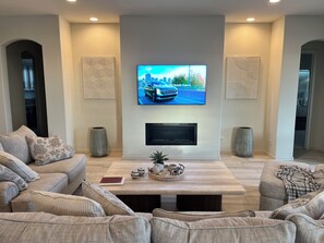 Un salon doté d’un téléviseur à écran plat fixé au mur, d’une cheminée en dessous et d’une table basse agrémentée d’objets décoratifs.
