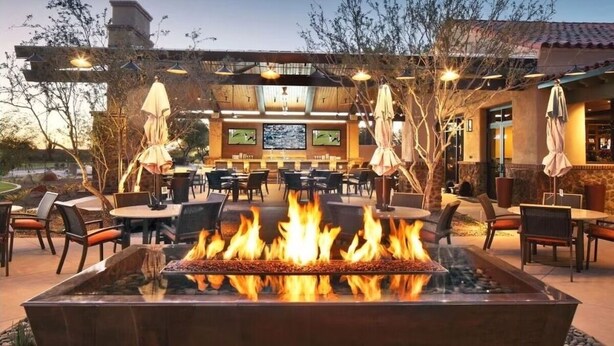 An outdoor patio with a fire feature, tables, chairs, and umbrellas.