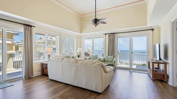 A spacious living room with a large beige sofa, a ceiling fan, and a view of the ocean through large windows.