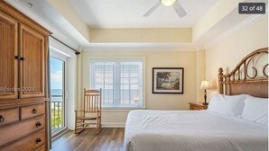 A bedroom with a bed, a wooden dresser, a rocking chair, a window with blinds, and a ceiling fan.