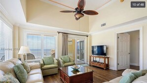 A spacious living room with a ceiling fan, a television on a wooden stand, and a large window with blinds.