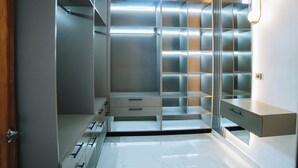 A modern, well-lit walk-in closet with built-in drawers, shelves, and hanging space, featuring a clean, minimalist design.