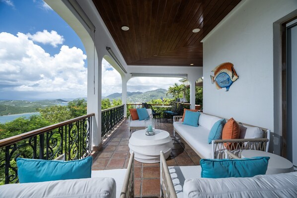 A balcony with a white sofa, blue cushions, a round white table, and a decorative fish wall art.