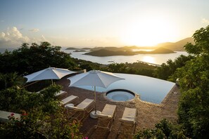 Ein Dachpool mit Infinity-Kante, Liegestühlen und Sonnenschirmen, umgeben von üppiger Vegetation mit Blick auf eine malerische Küstenlandschaft.