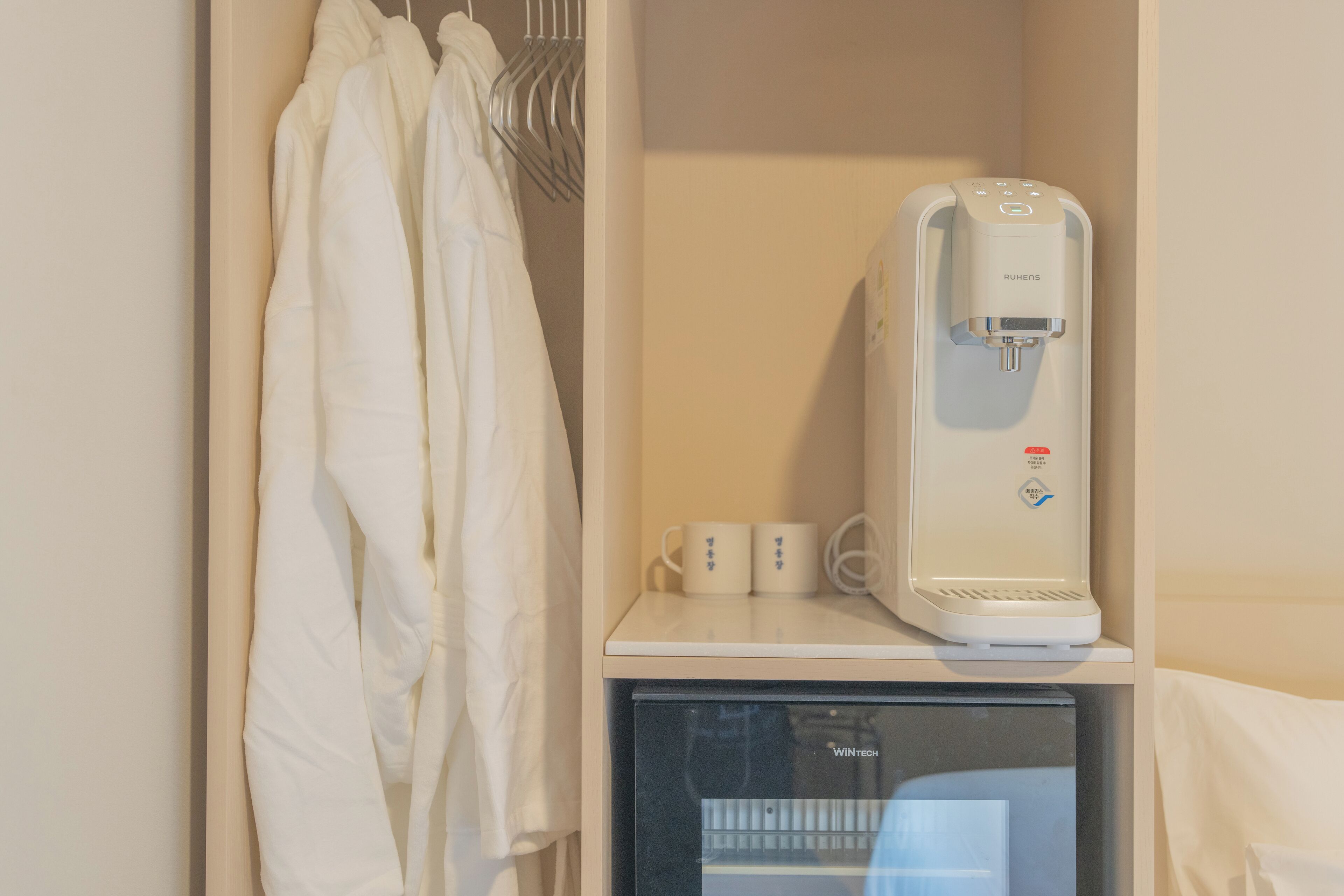 Een waterdispenser, een kleine koelkast en een ophangrek met handdoeken in een hotelkamer.